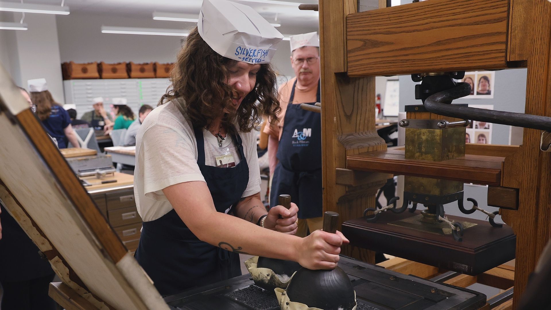Woman adds ink to a historic wooden printing press
